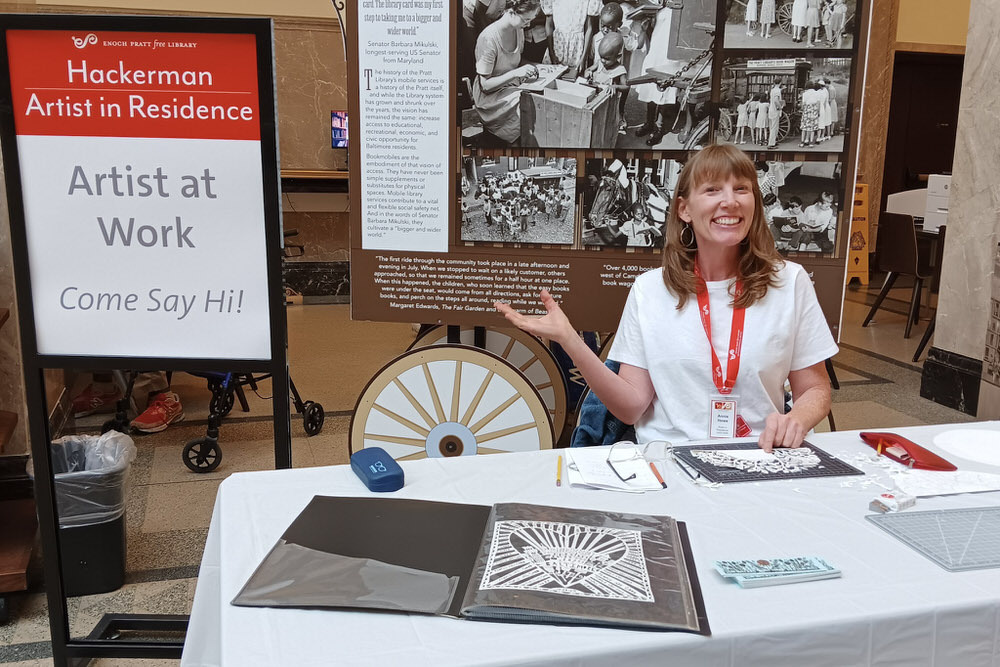 Annie Howe, artist working at the Central Library with Come Say Hi sign.